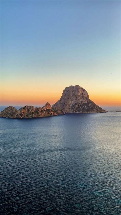 An Island In The Middle Of The Ocean At Sunset With One Large Rock