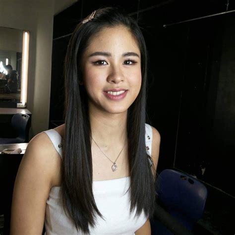 A Woman With Long Black Hair Wearing A White Top And Smiling At The Camera