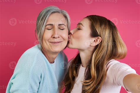 Adult Daughter Kissing Her Senior Mother While Making Selfie Against Pink Background 10177956