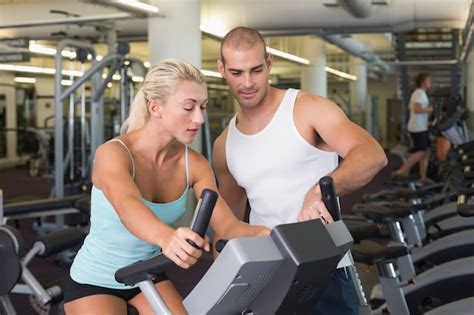 Premium Photo Trainer Assisting Woman With Exercise Bike At Gym