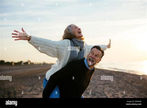 Cheerful Mature Woman Enjoying Piggyback Ride At Beach Stock Photo Alamy