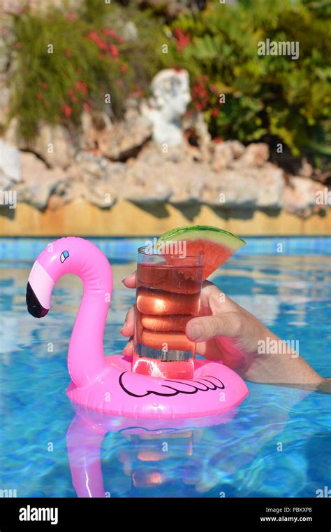 Woman’s hand , with a cocktail in an inflatable pink flamingo floating