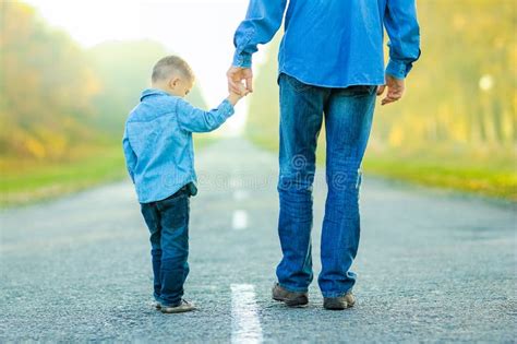 A Happy Parent With Child Are Walking Along The Road In The Park On