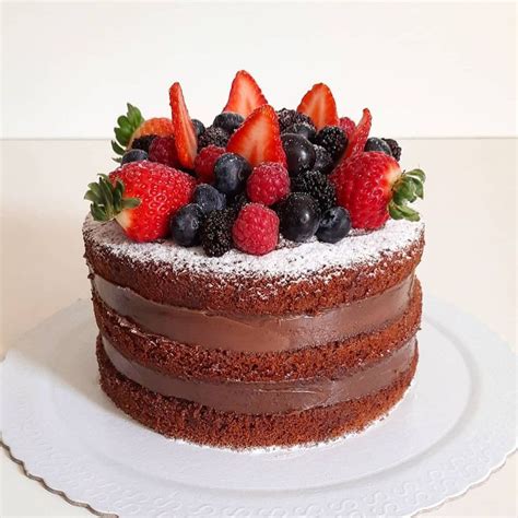 A Chocolate Cake Topped With Fresh Berries And Powdered Sugar On A