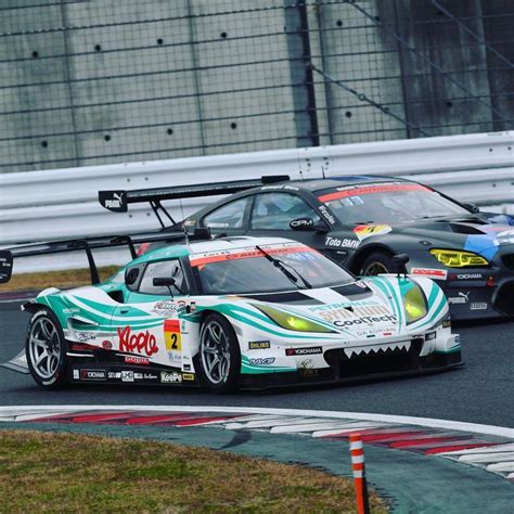 Two Racing Cars On A Race Track With One Driving Behind The Other In