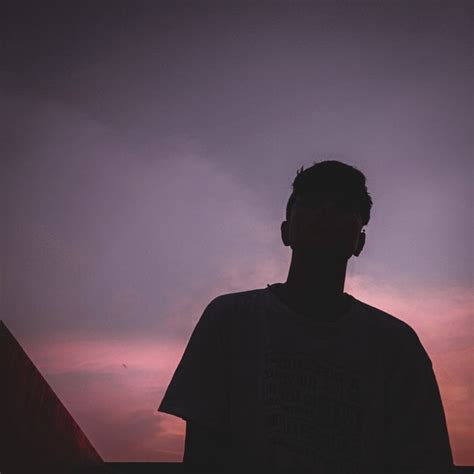 A Man Standing In Front Of A Pink And Purple Sky At Sunset With His