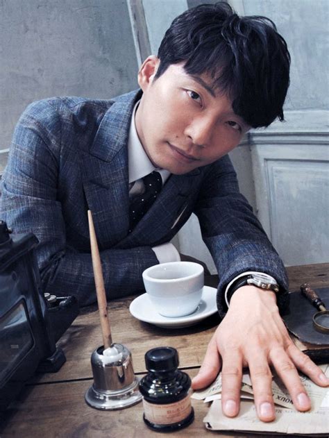 A Man In A Suit Sitting At A Table With His Hand Resting On The Book