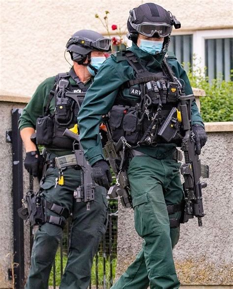 Two Police Officers Wearing Face Masks And Green Uniforms Walking Past