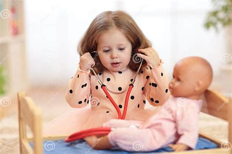 Two Years Old Girl Playing Doctor With Doll In The Nursery Stock Photo