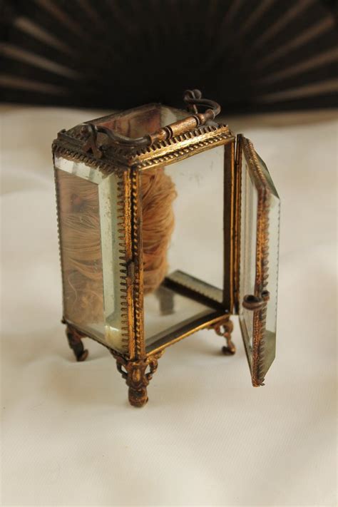 An Old Fashioned Glass And Metal Box On A White Surface