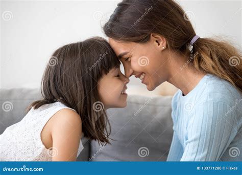 Mother And Daughter Touching With Foreheads Sitting On Couch Stock