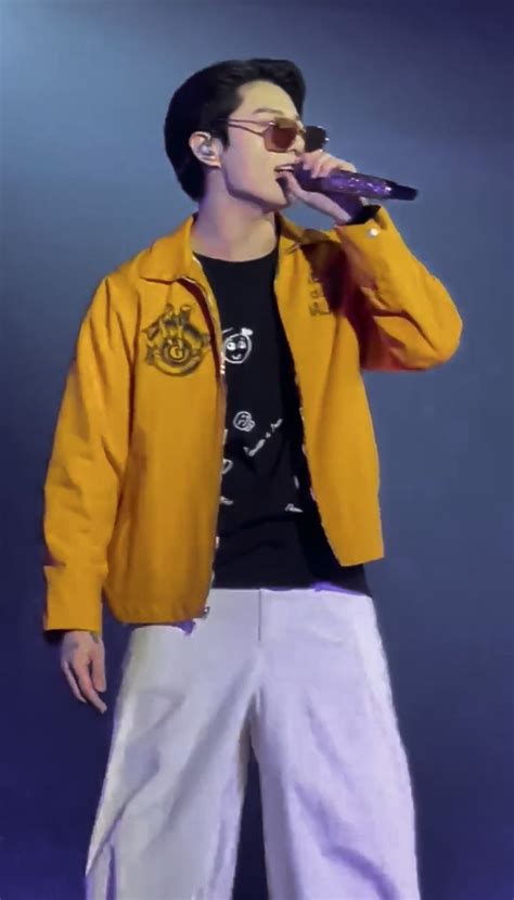 A Male In A Yellow Jacket And White Pants Is Singing Into A Microphone