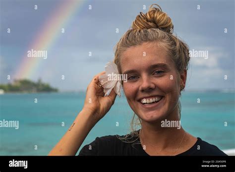 Une jeune femme blonde sourit tout en rentrant une fleur d hibiscus derrière son oreille avec