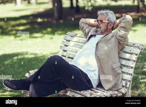 Portrait Of A Pensive Mature Man Sitting On A Bench In An Urban Park
