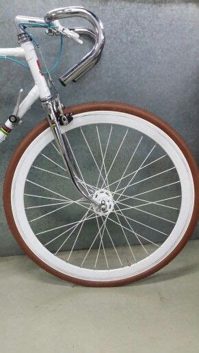 A White Bicycle With Brown Rims Parked Next To A Gray Wall And Cement Floor