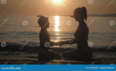 Silhouettes Mother And Daughter Sit On The Beach At Sunset Concept Of