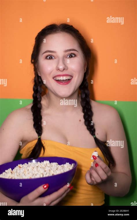 Charming Brunette Woman In Yellow Top Holding A Purple Bowl With Popcorn On Bright Green And