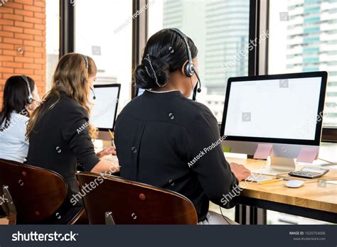 Businesswomen wearing headphones working on computers as telemarketing ...