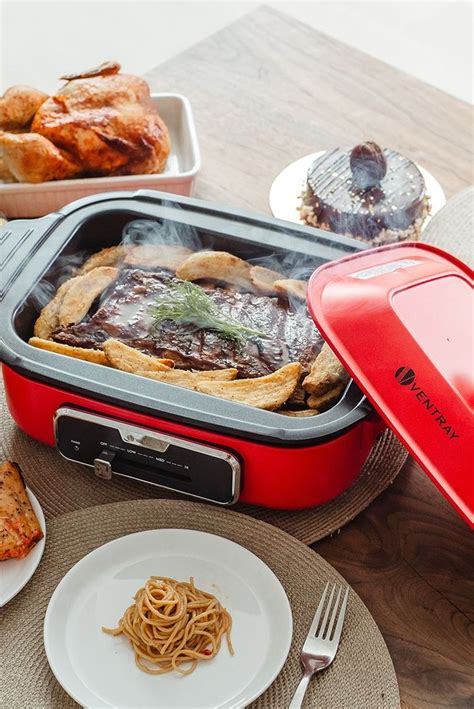 A Red And Gray Lunch Box With Food In It Sitting On A Table Next To