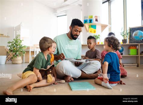 Group Of Small Nursery School Children With Man Teacher Sitting On