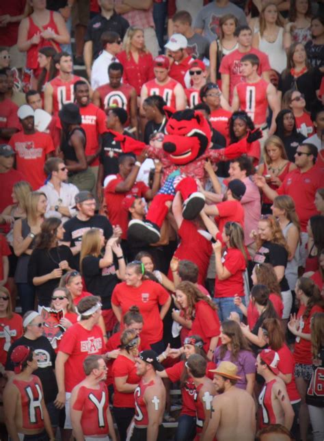 A Large Group Of People In Red Shirts And Black Shorts Standing Around