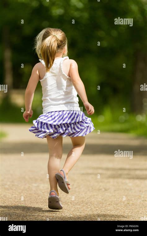 Young Female Child Skipping On A Rock Path In The Spring Time Back Is