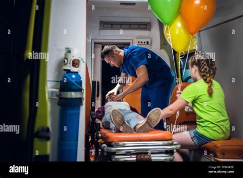 A Paramedic In A Blue Medical Uniform Regulates An Oxygen Mask On A