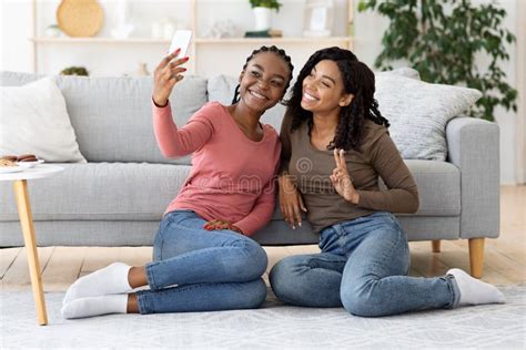 Two Black Girlfriends Gossiping While Sitting On Sofa At Home Stock