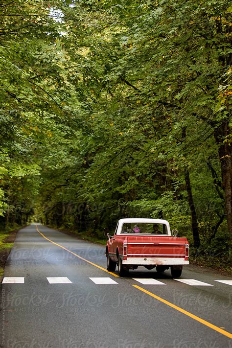 An Old Truck Driving Down A Long Straight Road In A Deciduous Forest By Stocksy Contributor