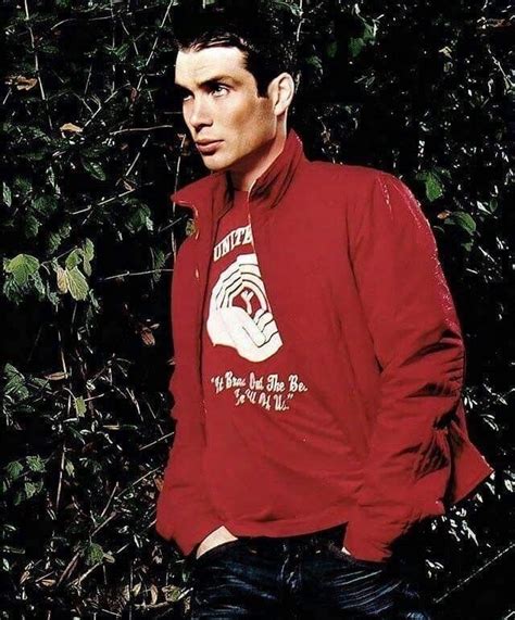 A Man Standing In Front Of Some Bushes Wearing A Red Shirt And Jeans