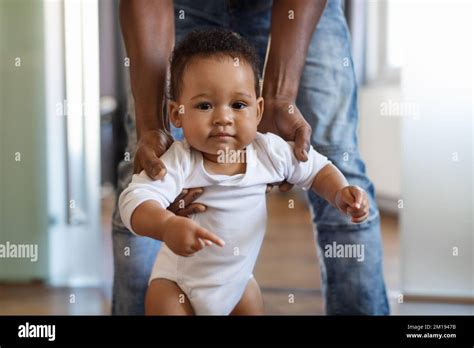 Portrait Of Adorable Little Black Baby Walking With Fathers Help In