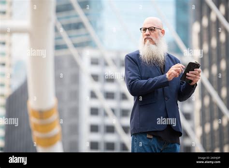 Mature Bearded Bald Businessman Thinking While Using Phone In The City