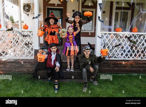 multiethnic kids in halloween costumes grimacing and showing scary gestures near decorated ...