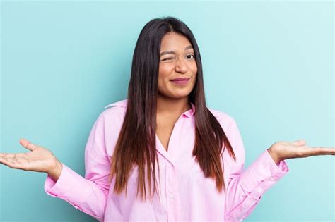 Joven venezolana aislada sobre fondo azul dudando y encogiéndose de