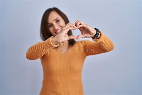 Middle Age Brunette Woman Standing Wearing Orange Sweater Smiling In Love Doing Heart Symbol