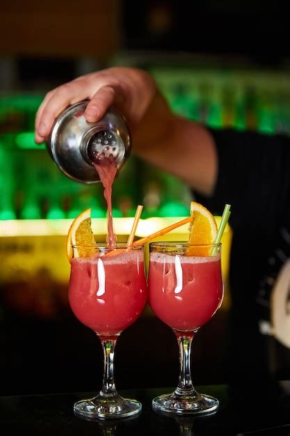 Premium Photo The Bartender Pours An Alcoholic Cocktail From A Shaker Into Glasses Decorated