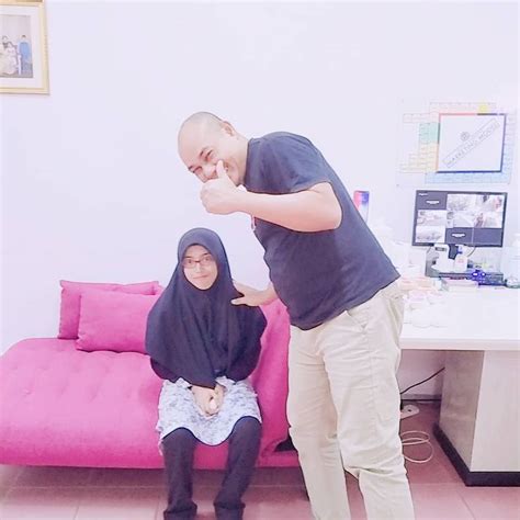 A Man Standing Next To A Woman Sitting On A Pink Couch In Front Of A Desk