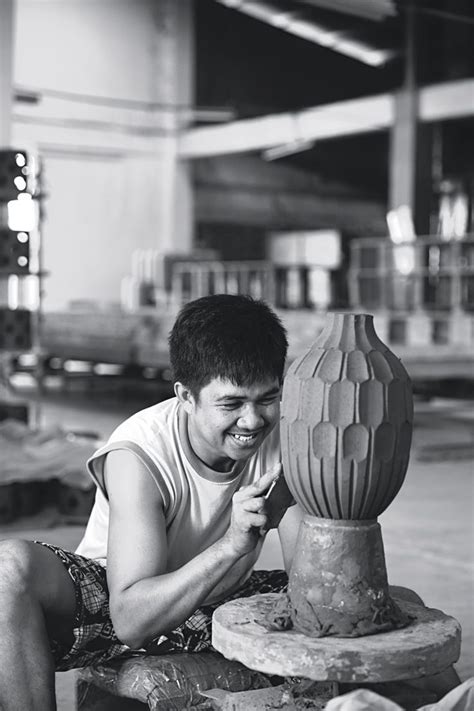 A Man Sitting On The Ground Next To A Large Vase With A Flower In It