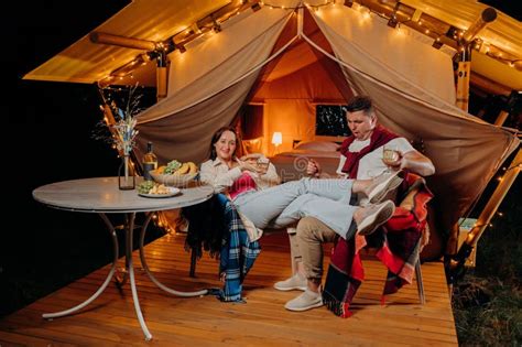 Happy Funny Couple Relaxing In Glamping On Summer Evening And Drinking