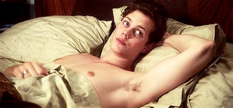 A Shirtless Man Laying In Bed Looking At The Camera