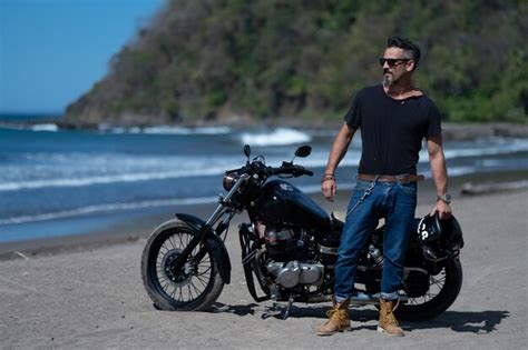 Hombre Con Barba Y Gafas De Sol Junto A Su Moto En La Playa Foto Premium