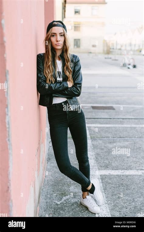 Fashionable Young Woman Wearing Baseball Cap Leaning Against Wall Stock