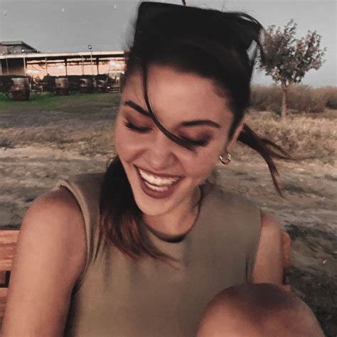 A Woman Sitting On Top Of A Wooden Bench Next To A Building And Smiling