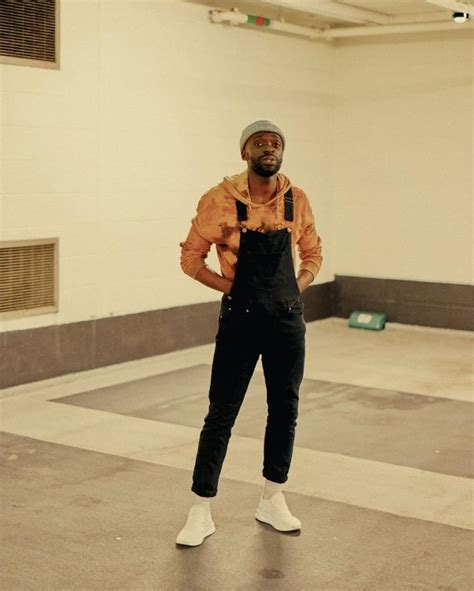 A Man Standing In An Empty Room With His Hands On His Hips Wearing Overalls