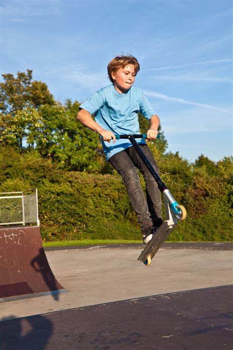 O Menino Salta Seu Trotinette Do Truque No Skatepark Foto De