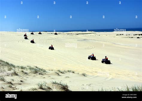 Happy quad bikers driving in sand dunes at Anna bay (Newcastle, NSW, Australia). Active people ...