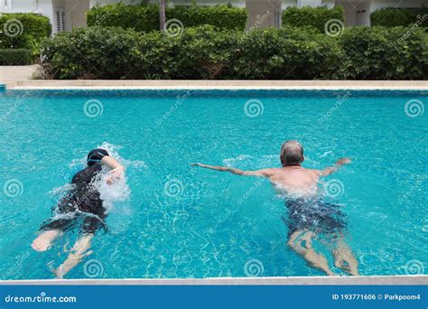 Happy Elderly Caucasian Husband And Elderly Asian Wife Swimming In Pool During Retirement