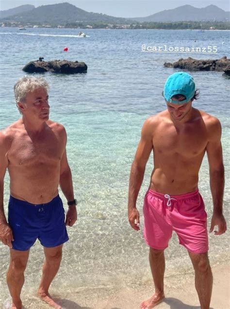 Two Men Standing On The Beach Next To Each Other Wearing Blue And Pink