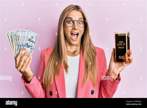 Jeune femme blonde portant le style d affaires tenant lingots d or et dollars célébrant fou et