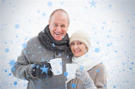 Premium Photo Happy Mature Couple In Winter Clothes Holding Mugs Against Snow Falling